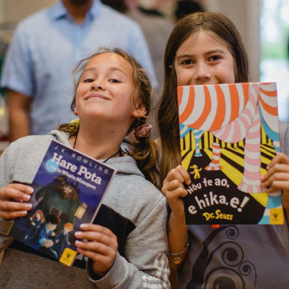 Two girls smiling for a photo with the Hare Pota and Nōu te Ao pukapuka